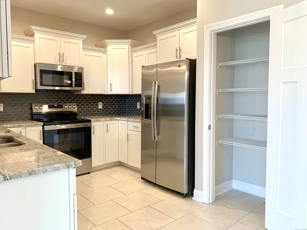 a kitchen with stainless steel appliances granite countertop a refrigerator a stove a sink and white cabinets