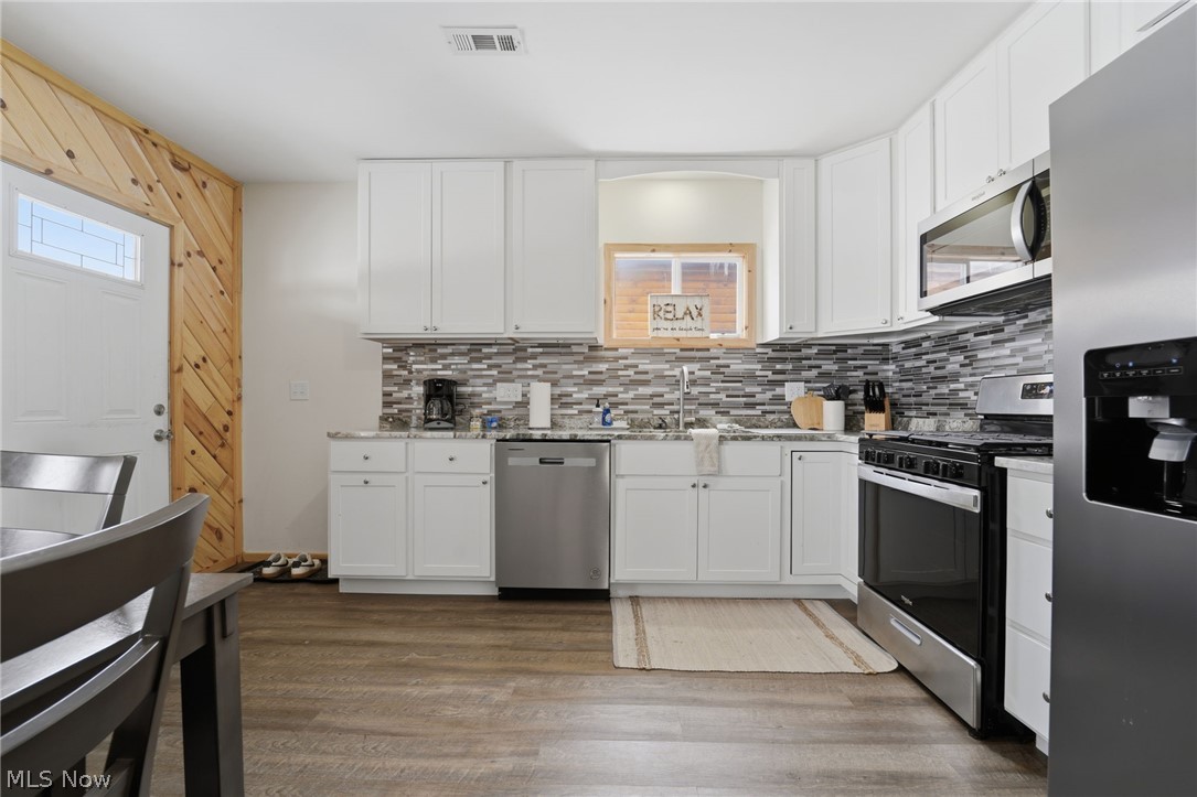 5919 Lake Road West, Unit 32 Ashtabula, OH 44004 - Photo 6 of 23 Kitchen featuring stainless steel appliances, white cabinetry, light wood-style floors, healthy amount of natural light, and wood walls