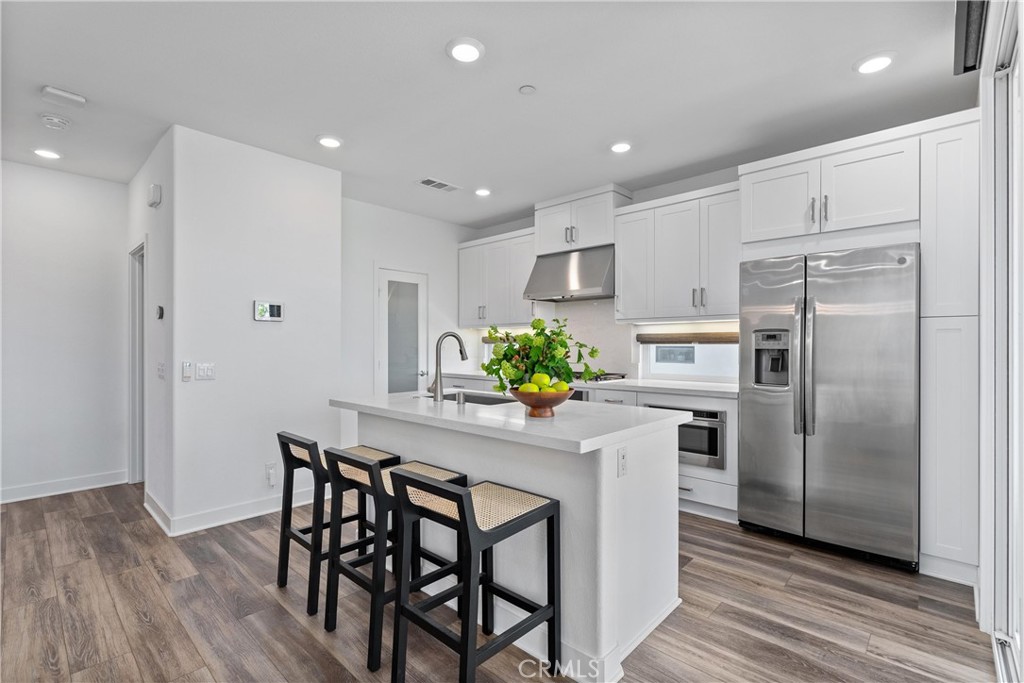 303 Lodestar Tustin, CA 92782 - Photo 9 of 37 a kitchen with stainless steel appliances a refrigerator a stove a sink and white cabinets with wooden floor