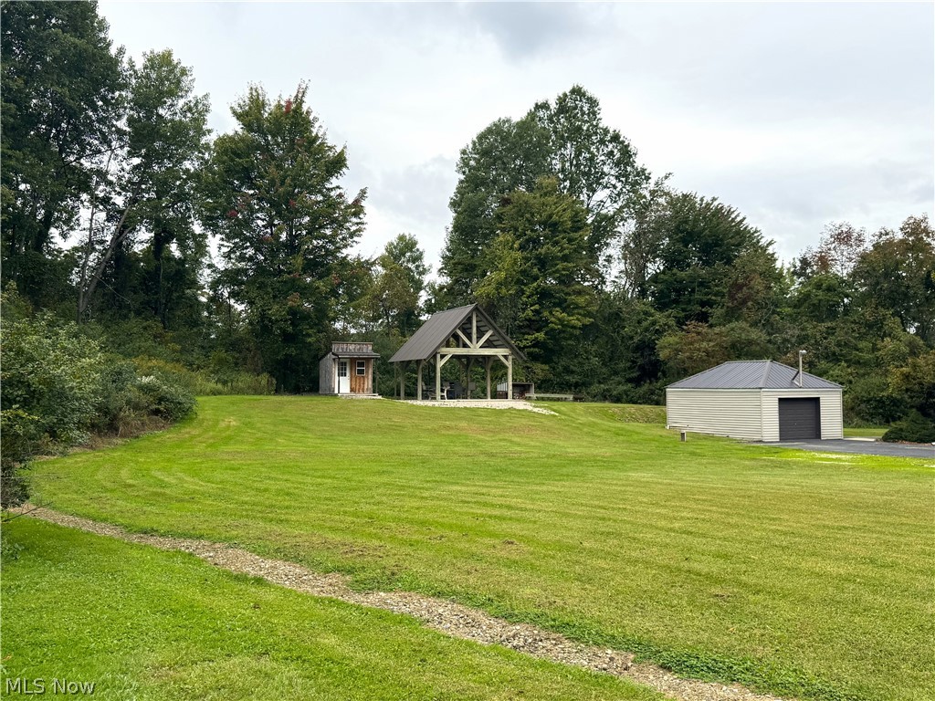 4421 State Road South Ashtabula, OH 44004 - Photo 3 of 18 Expansive grassy terrain featuring a detached garage with a roll-up door, a separate wooden shed, and an open-air structure with a vaulted ceiling