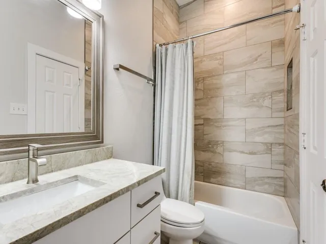 a bathroom with a granite countertop bathtub shower sink vanity and toilet