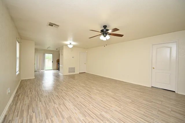 a view of an empty room with wooden floor and a ceiling fan