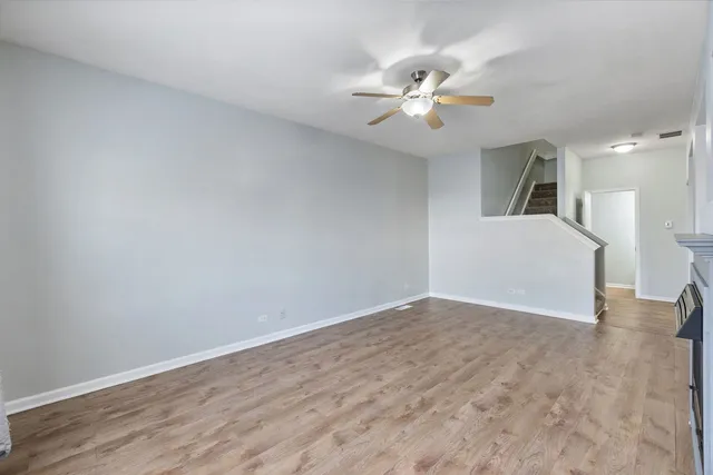 a view of an empty room with wooden floor and a ceiling fan