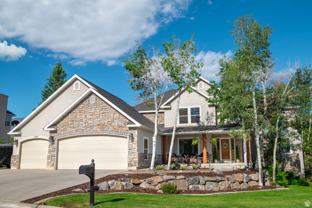 Craftsman-style home with an attached garage, stone siding, driveway, stucco siding, and a large covered porch
