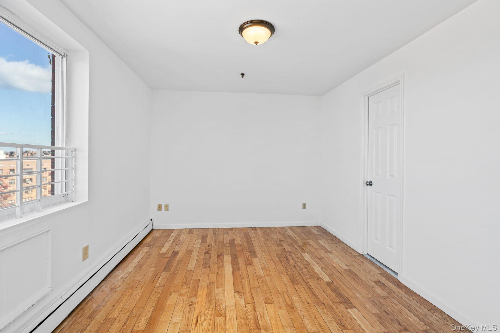 136-16 31st Road, Unit 8B Queens, NY 11354 - Photo 12 of 23 Empty room featuring a baseboard heating unit and light wood-type flooring