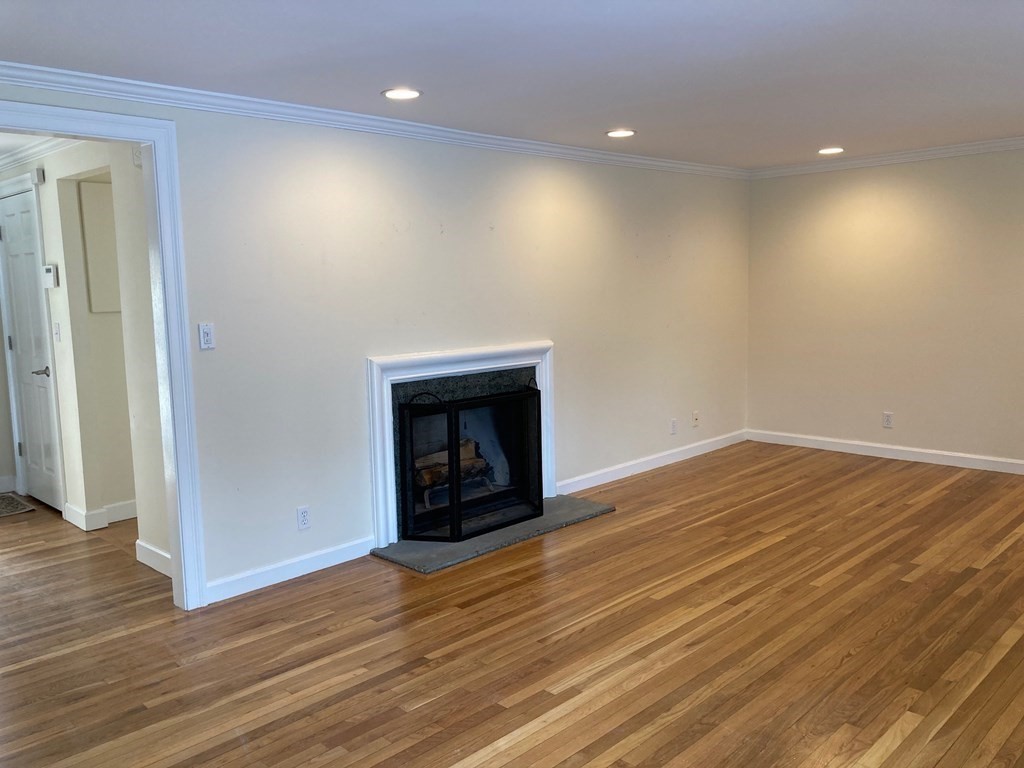 114 Jericho Road, Unit 114 Weston, MA 02493 - Photo 4 of 9 an empty room with wooden floor and fireplace