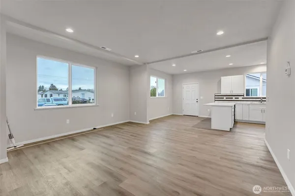 a view of an empty room with wooden floor and a kitchen