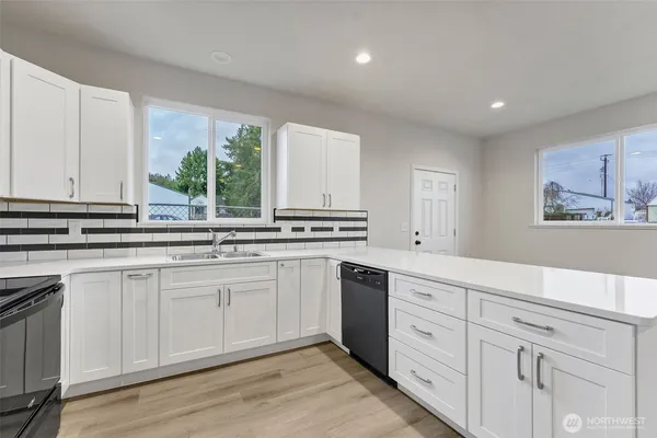 a large white kitchen with stainless steel appliances granite countertop a stove a microwave oven a refrigerator a sink and dishwasher with wooden floor