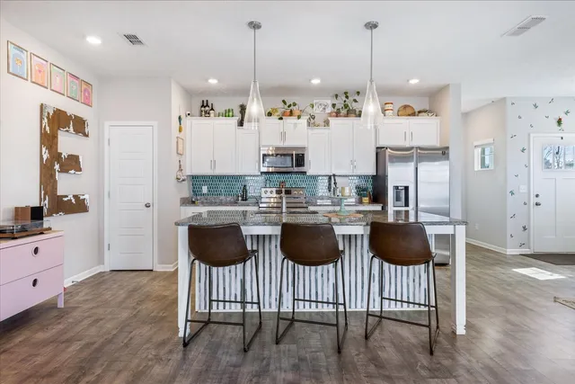 a kitchen with stainless steel appliances granite countertop a stove a sink a refrigerator and white cabinets with wooden floor