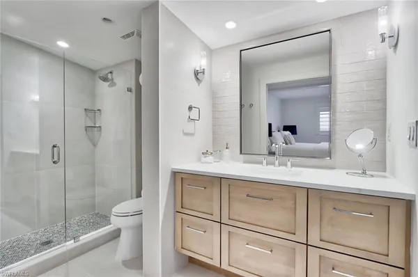 a bathroom with a toilet a sink a glass door a shower a mirror a vanity and shower