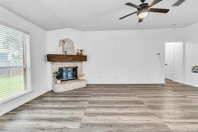 a view of a livingroom with a fireplace a ceiling fan and wooden floor