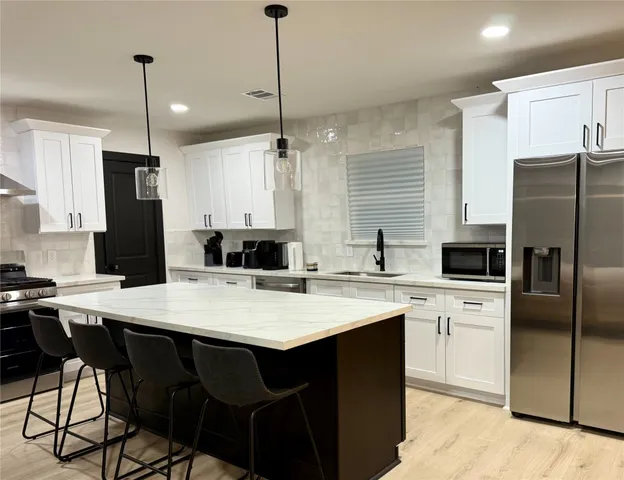 a kitchen with stainless steel appliances granite countertop a refrigerator a sink a stove a kitchen island with chairs and white cabinets