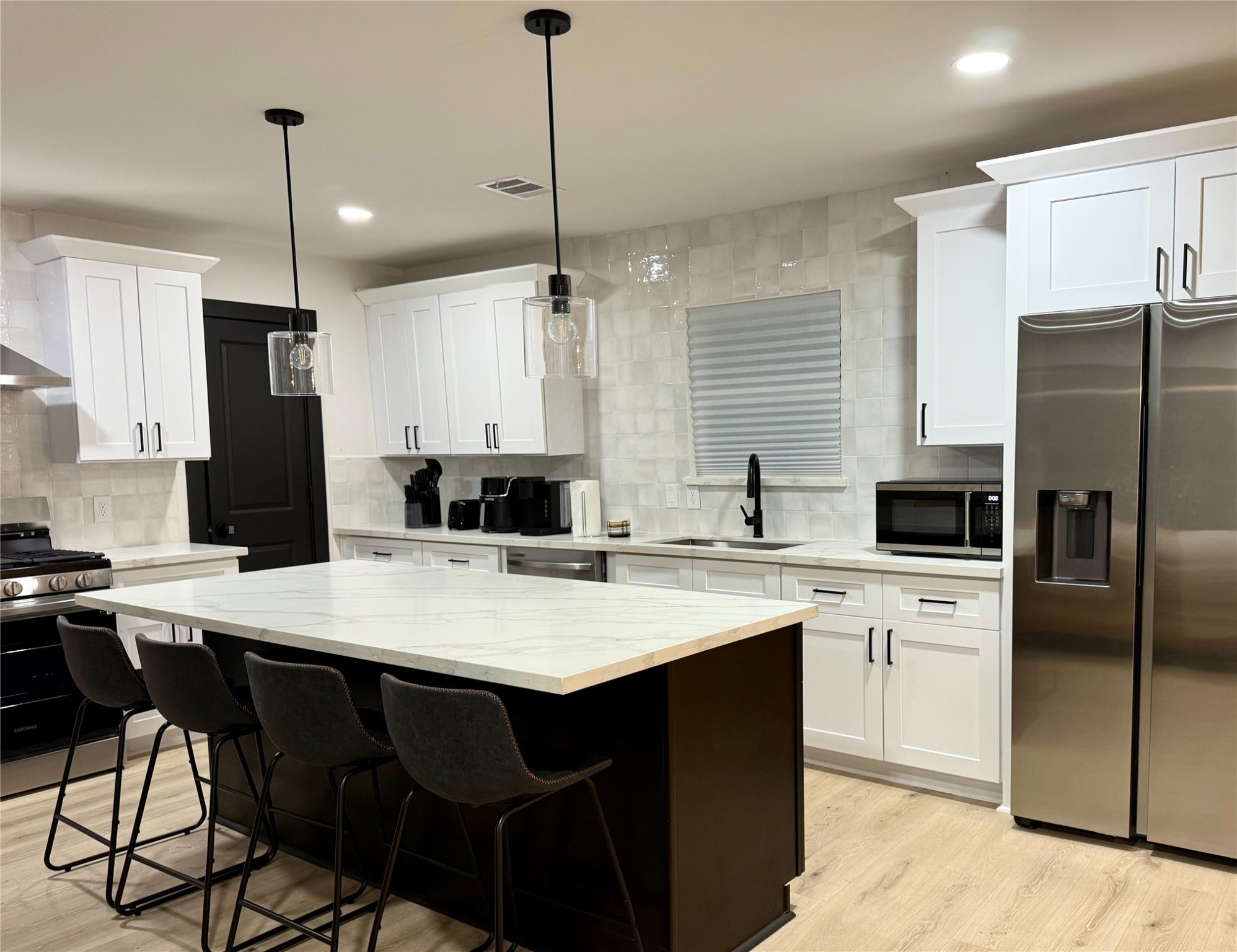 6305 Gay Street Houston, TX 77022 - Photo 6 of 13 a kitchen with stainless steel appliances granite countertop a refrigerator a sink a stove a kitchen island with chairs and white cabinets