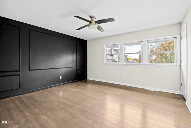 a view of an empty room with wooden floor and a ceiling fan