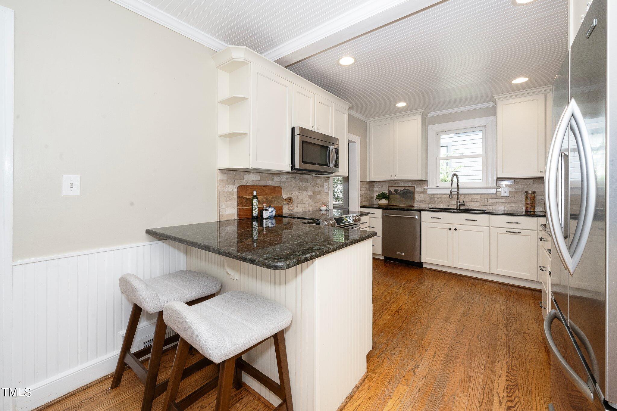 406 Brooks Avenue Raleigh, NC 27607 - Photo 14 of 33 a kitchen with stainless steel appliances granite countertop a sink a stove a refrigerator cabinets and a dining table with wooden floor