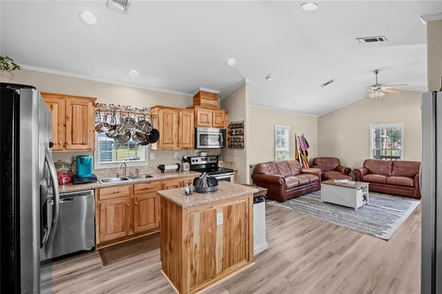 a living room with stainless steel appliances a kitchen island hardwood floor sink stove and wooden cabinets