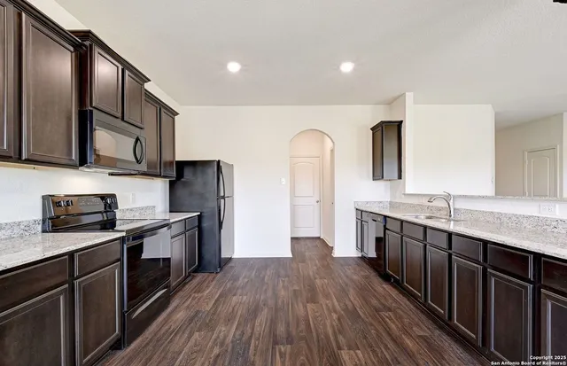 a kitchen with stainless steel appliances granite countertop wooden cabinets a sink dishwasher a stove and a refrigerator with wooden floor