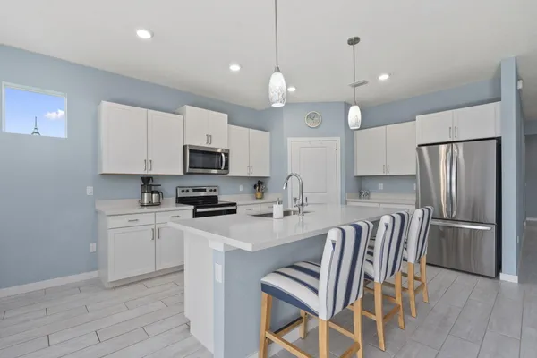 a kitchen with stainless steel appliances granite countertop a stove a sink a microwave a refrigerator with white cabinets and wooden floor