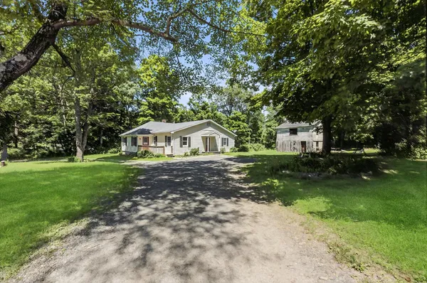 a white house with a big yard plants and large trees