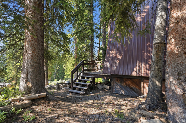 8505 South Snake Crk Road Salt Lake City, UT 84121 - Photo 44 of 67 Wood-sided structure with a metal roof surrounded by mature trees, featuring an exterior wood staircase and elevated decking