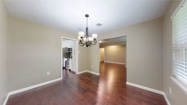 an empty room with wooden floor chandelier and windows