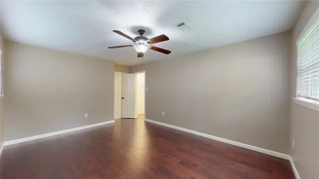 an empty room with wooden floor fan and windows