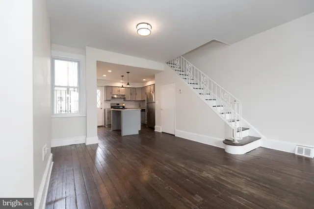 an empty room with wooden floor staircase and windows