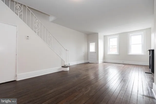 a view of an empty room with wooden floor and fan