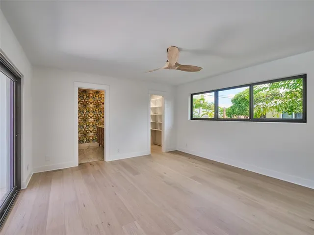 a view of an empty room with wooden floor and a ceiling fan