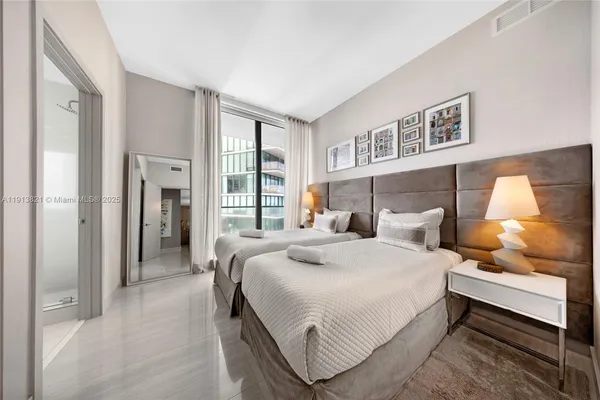 a bedroom with a bed and a lamp on dresser with wooden floor