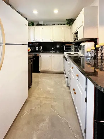 a kitchen with granite countertop a refrigerator a sink and white cabinets