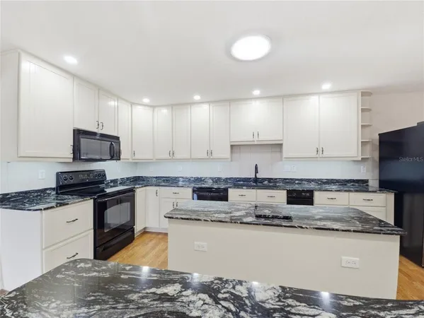 a kitchen with granite countertop a sink a stove top oven a counter space and cabinets