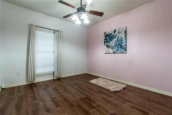 an empty room with wooden floor chandelier fan and windows