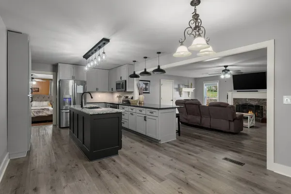 a large living room with stainless steel appliances kitchen island granite countertop furniture a fireplace and a chandelier