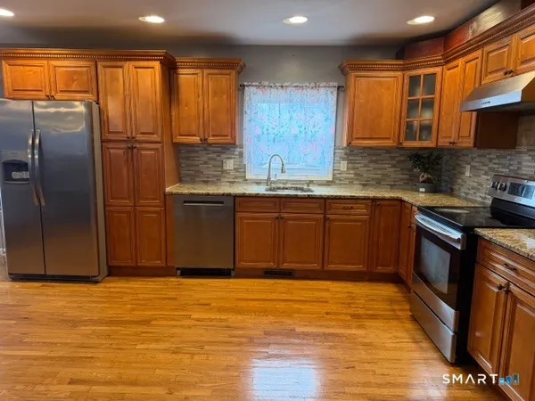 a large kitchen with stainless steel appliances granite countertop a refrigerator a sink dishwasher a dining table and chairs with wooden floor