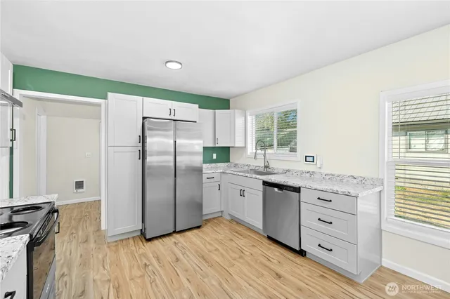 a kitchen with granite countertop a refrigerator a sink dishwasher a stove and white cabinets with wooden floor