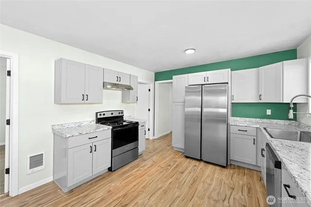 a kitchen with stainless steel appliances granite countertop a refrigerator a sink dishwasher a stove and white cabinets with wooden floor