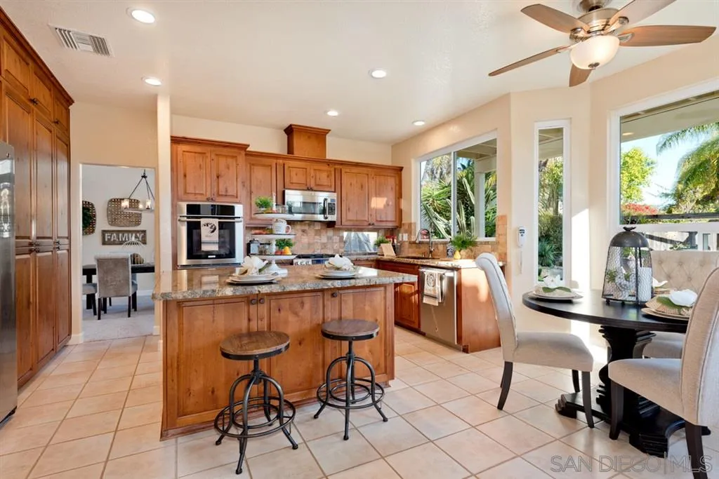 7675 Salix Place San Diego, CA 92129 - Photo 8 of 25 a kitchen with stainless steel appliances kitchen island granite countertop a stove a refrigerator a kitchen island a couches and a dining table with wooden floor