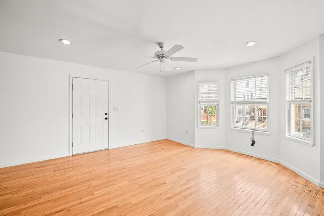 an empty room with chandelier fan and windows
