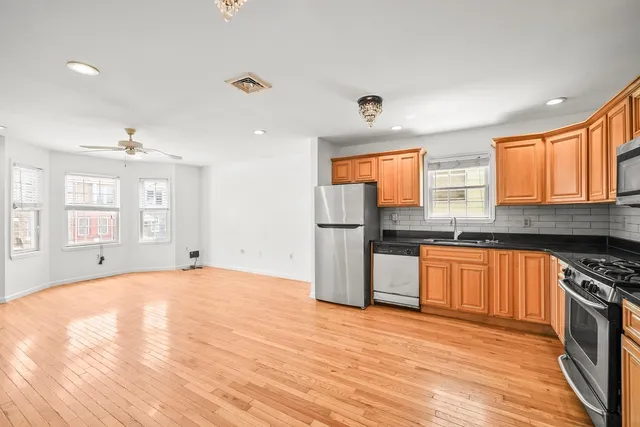 a kitchen with stainless steel appliances granite countertop a refrigerator a sink dishwasher a stove and a dining table with wooden floor