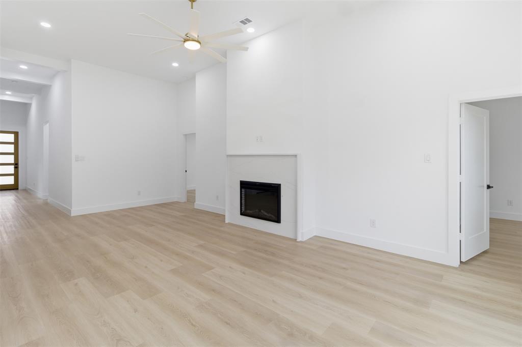 1115 Riverwood Road Dallas, TX 75217 - Photo 10 of 39 Unfurnished living room with light wood finished floors, ceiling fan, recessed lighting, a glass covered fireplace, and a towering ceiling