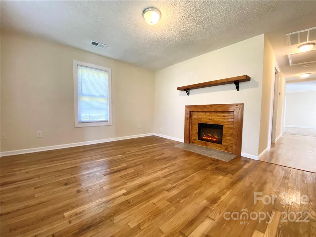 3367 Deerbrook Road Lenoir, NC 28645 - Photo 4 of 13 an empty room with wooden floor a fireplace and windows