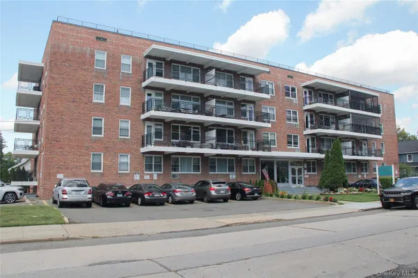 a front view of a building with lot of cars and trees
