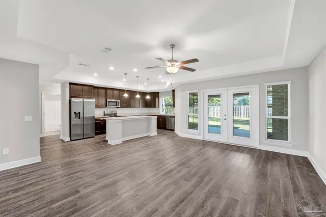 a view of an empty room with wooden floor and a kitchen