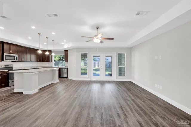 a view of an empty room with wooden floor and a kitchen