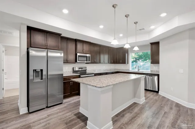 a large kitchen with a center island wooden floor stainless steel appliances and windows