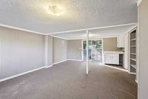 a view of an empty room with a window and a kitchen