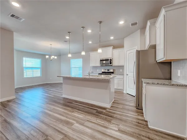 a kitchen with stainless steel appliances kitchen island granite countertop a stove a refrigerator and white cabinets with wooden floor