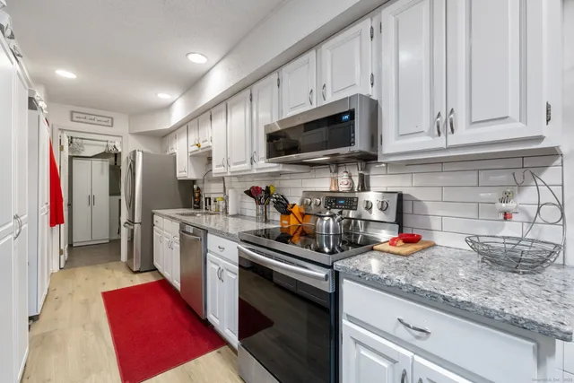 a kitchen with stainless steel appliances granite countertop a refrigerator a sink dishwasher and white cabinets with wooden floor