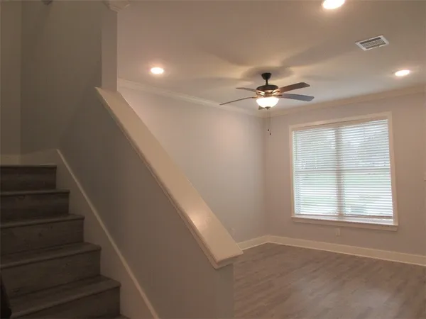 a view of an empty room with wooden floor and a ceiling fan